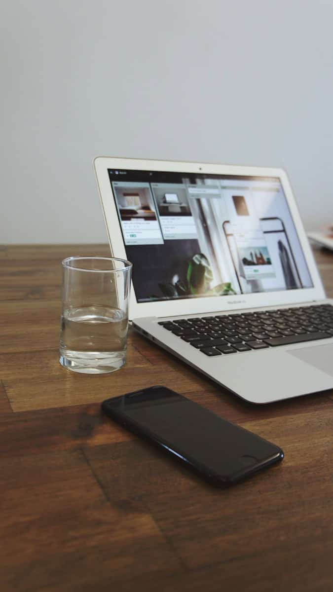 clear glass and iPhone beside turned on MacBook