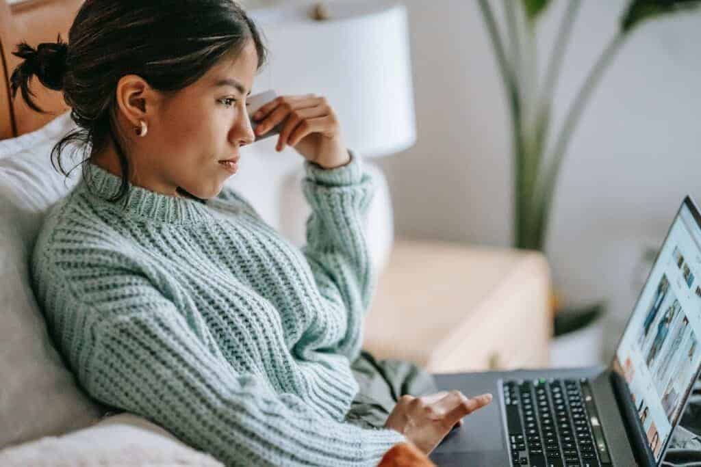 Side view of crop concentrated young ethnic female using touchpad of netbook and shopping online