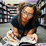 woman in black, blue, and red shirt lying on surface while reading magazine