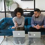 a man and woman sitting on a couch with their laptops